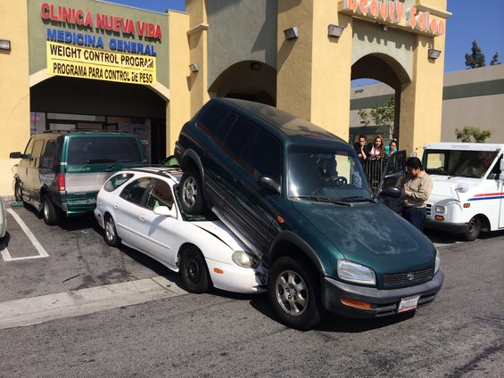 Green SUV on top of white sedan in parking lot