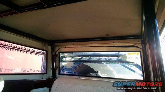 Interior view looking out rear window, showing roll cage and roof liner. Stickers visible on rear window
