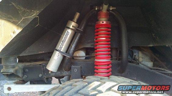 Close-up of a silver "RaceRunner" shock absorber and a red coilover shock mounted on an off-road vehicle's suspension system