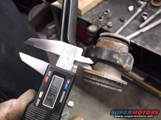 Digital calipers measuring a rusty suspension component. The display reads 106.4
