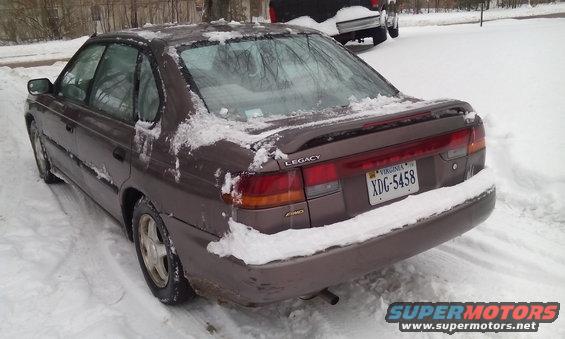 Brown 1996 Subaru Legacy sedan parked in snow, rear 3/4 view, snow on body and ground