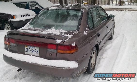 1996 Subaru Legacy sedan parked in snow, rear 3/4 view. Another vehicle is partially visible to the left
