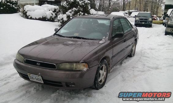 1996 Subaru Legacy sedan parked in snow, front quarter view. Other vehicles visible in background