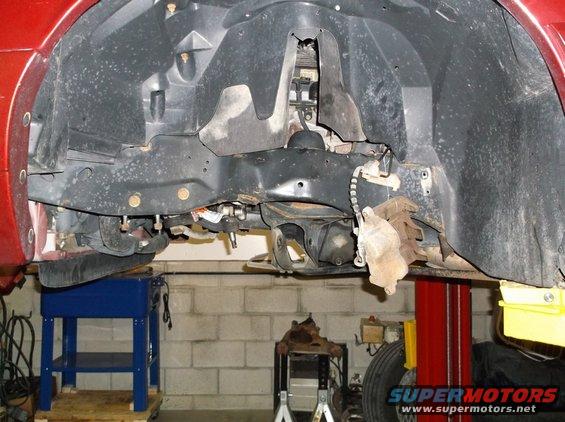 Red vehicle's front undercarriage, showing suspension and brake components, lifted on a red car lift