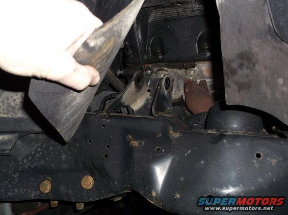 Close-up of engine block, exhaust manifold, and frame structure with a hand holding a black rubber piece