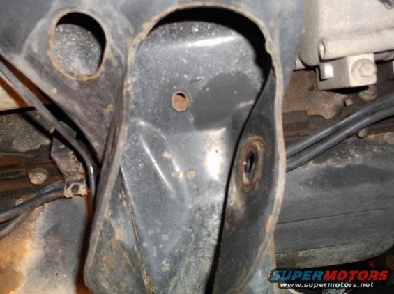 Close-up of rusted metal bracket with holes and attached black hoses