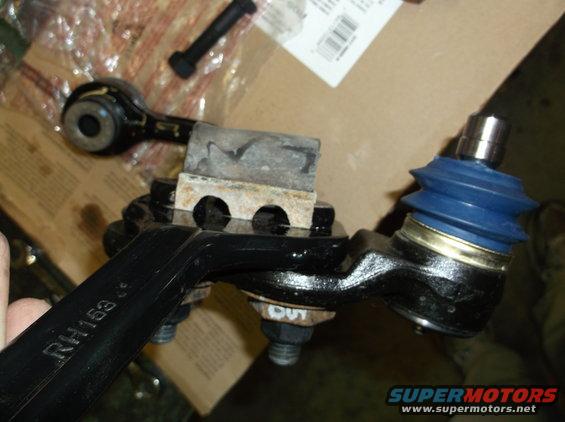 Close-up of a suspension ball joint with a blue rubber boot and a metal arm labeled RH153