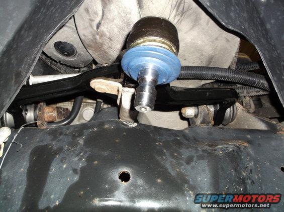 Ball joint with blue boot attached to black suspension arm, viewed from below
