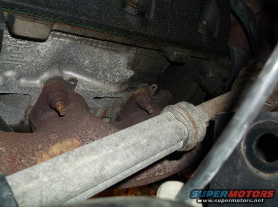 Close-up of a rusty exhaust manifold and a metal pipe, likely from a vehicle engine bay