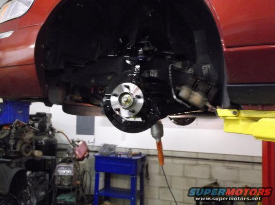 Red car's front wheel assembly with brake rotor and caliper visible, lifted on a yellow jack