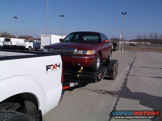 Red 1999 Mercury Grand Marquis on a trailer, being towed by a white pickup truck