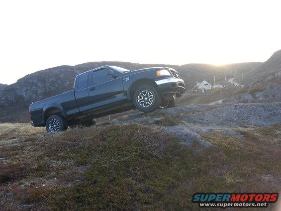 Dark Ford F-150 truck driving up a rocky hill with houses in the background