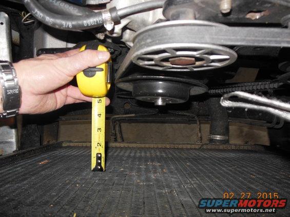 Hand holding tape measure near engine belt and pulley system over radiator