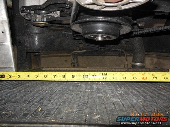 Close-up of engine belts and pulleys above a radiator with a tape measure