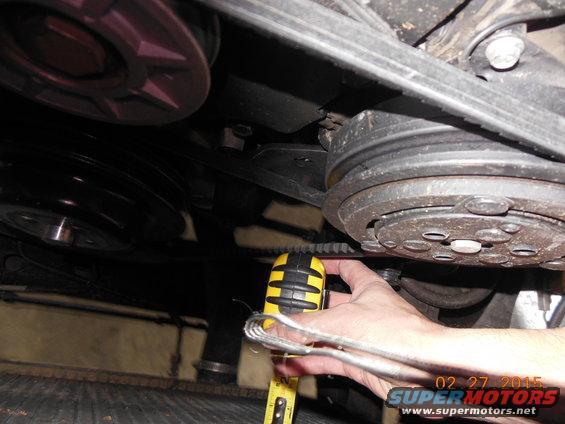 Close-up of a hand measuring a car's serpentine belt near the AC compressor pulley