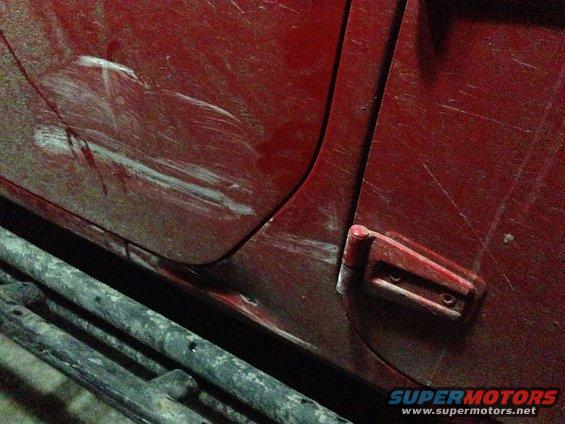 Red vehicle door with significant scratches and a visible side step