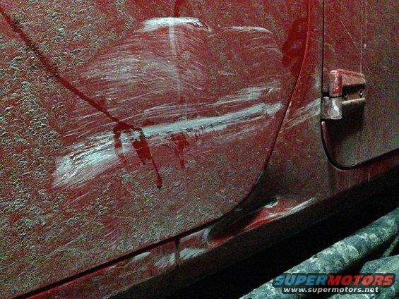 Close-up of a red vehicle door with deep scratches and some white paint transfer