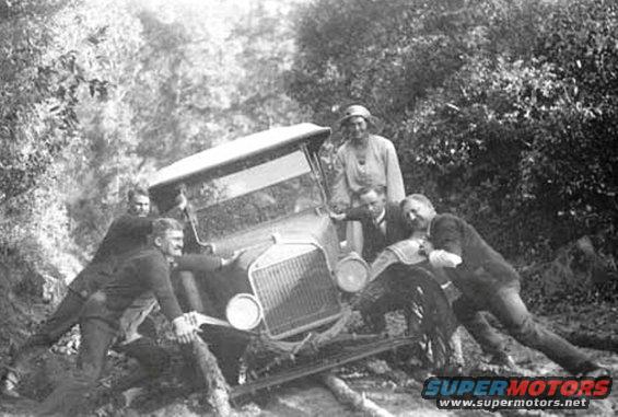 1909 Ford Model T stuck in mud, being pushed by five men and one woman