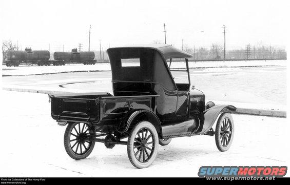 1923 Ford Model T truck, rear view. The truck has a black soft top and a wooden bed. Two tank cars are visible in the background