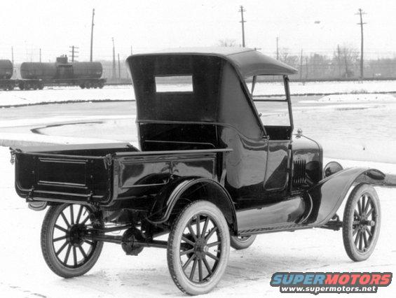 Rear three-quarter view of a black 1917 Ford Model T pickup truck with a soft top, parked in a snowy area near train cars