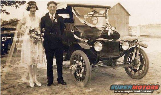 Wedding couple poses with a vintage car decorated with ribbons