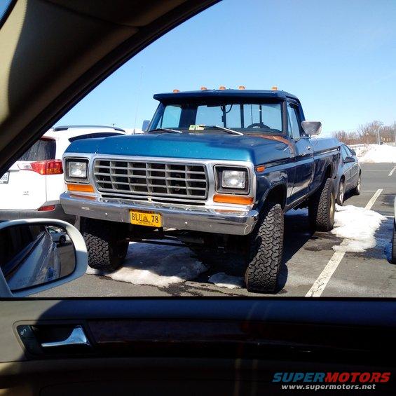 Blue pickup truck with lifted suspension and large tires. Yellow license plate reads 'BLLU 78'