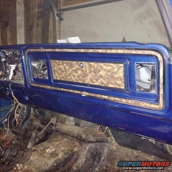 Blue dashboard with woodgrain trim and exposed wiring. Floor is dirty with pedals visible
