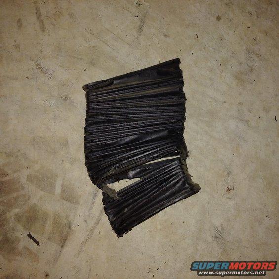 Torn black rubber bellows with accordion folds, lying on a concrete floor