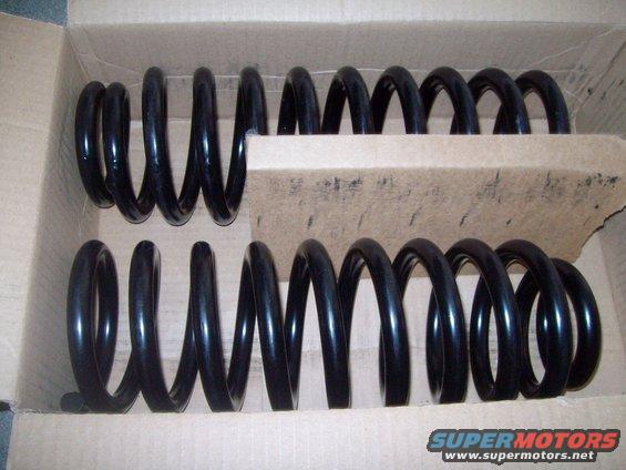 Two black coil springs in a cardboard box. The springs appear to be new replacement parts