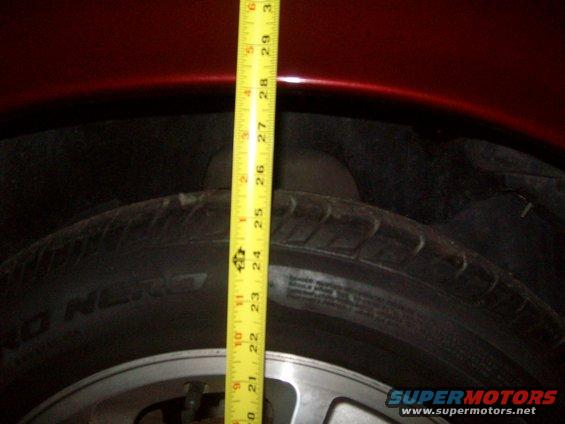 Red fender over tire, measuring suspension height with a tape measure