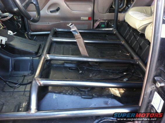 Interior view of a vehicle showing a custom roll cage installed over the floor and seats