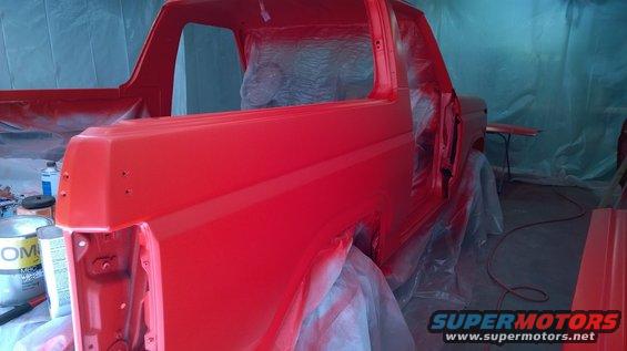 1983 Ford Bronco in a paint booth, covered in plastic, being sprayed red