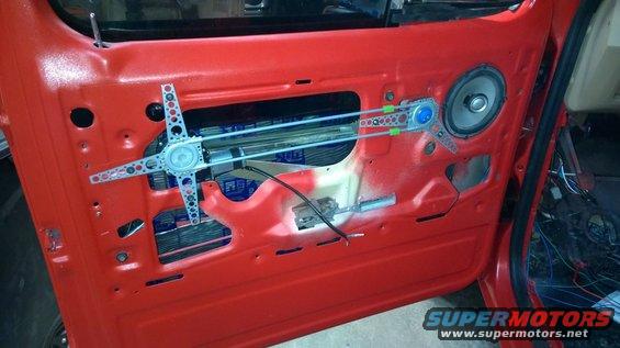 Red vehicle door interior with window mechanism, speaker, and wiring visible