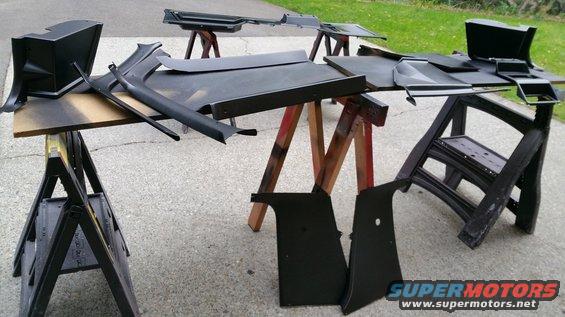 Various black plastic car interior trim pieces drying on sawhorses outdoors