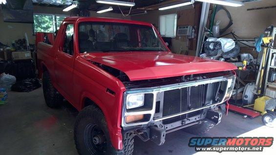 Red SUV with hood open, missing grille and bumper, parked in a garage