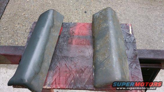 Two dark gray bumper end caps resting on a piece of plywood with red spray paint
