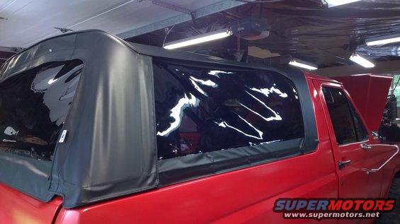 Red 1983 Ford Bronco with black soft top and clear plastic windows, parked indoors