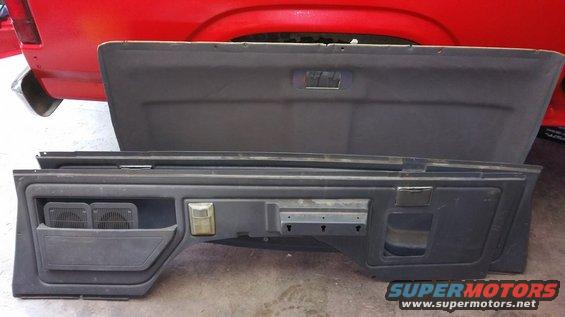 Dark gray interior panels, one with speaker grilles and a light, are laid out in front of a red vehicle's rear section