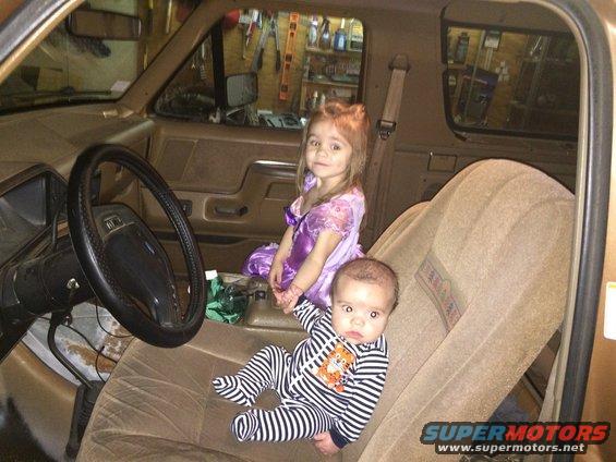 Interior of a 1991 Ford Bronco with a baby and a young girl sitting on the passenger seat and dashboard
