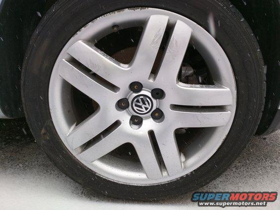Close-up of a silver Volkswagen wheel with the VW logo in the center. The tire is black and the ground is covered in snow