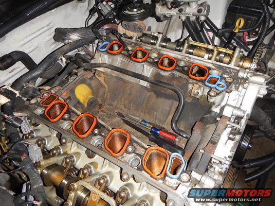 Engine intake manifold removed, showing gaskets and internal components. Tools are present