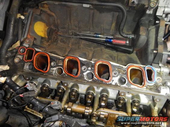 Engine intake manifold removed, showing ports and gasket mating surface. Tools are visible in the background