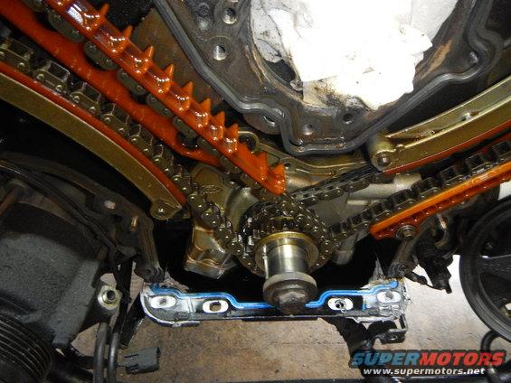 Engine timing chain and guides disassembled, showing metal sprockets and orange plastic tensioners