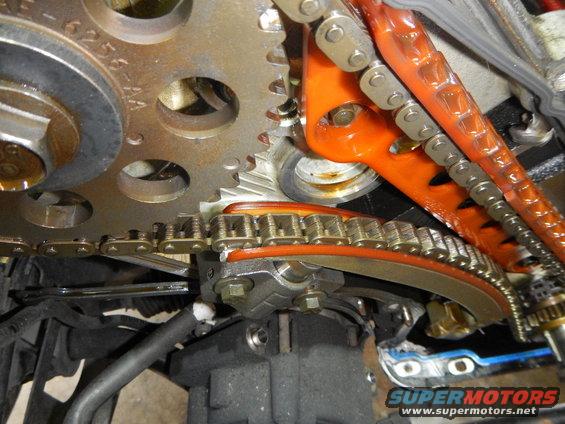 Close-up of engine timing chain, gears, and orange tensioner guide