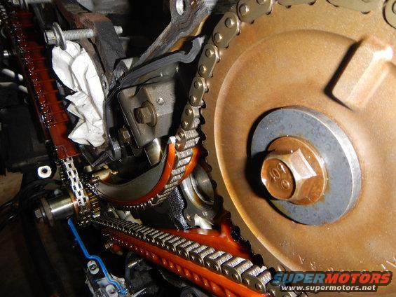Engine timing chain and gears with orange plastic guides and a large bolt on a rusty gear