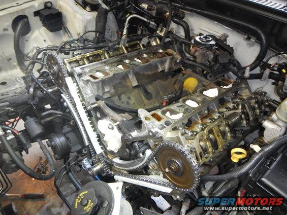 Disassembled engine with timing chains and gears exposed, showing internal components and wiring