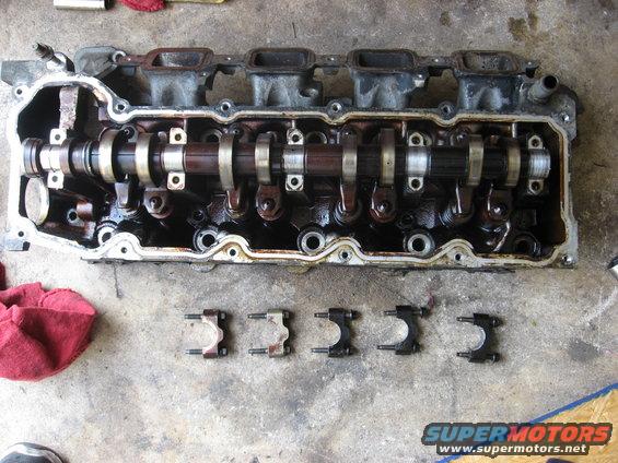 Engine cylinder head with camshaft and rocker arms removed, some parts laid out on concrete