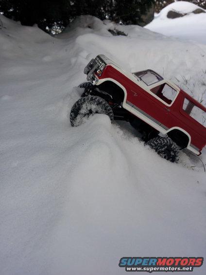 Red and white remote control truck driving through snow