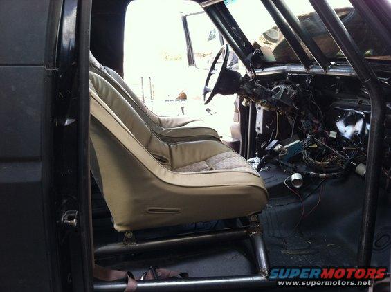 Interior of a vehicle with racing seats, roll cage, and exposed wiring