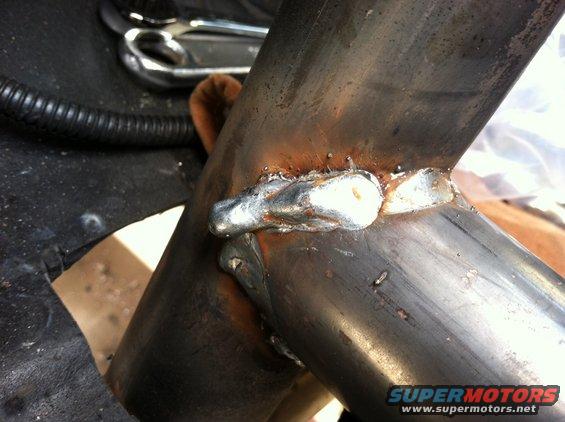 Close-up of welded metal pipes, possibly part of a vehicle's exhaust or frame. A Supermotors.net watermark is visible